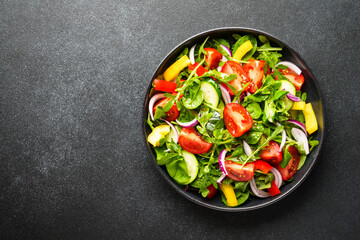 Green salad with fresh leaves and vegetables. Top view on black.