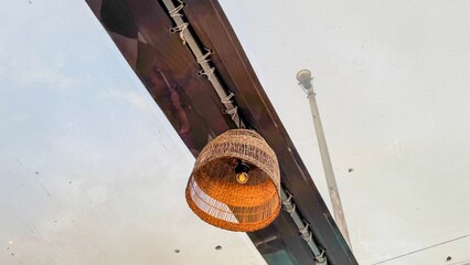 Woven wicker lantern glows warmly against cloudy sky, celebrating Hygge season with a hint of...