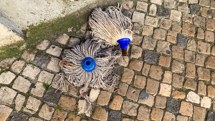 Weathered mops rest on cobblestones, echoing Tavern Day nostalgia and peculiar celebrations of...