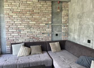 Living room interior, large corner gray sofa with pillows, brick and concrete walls, loft style