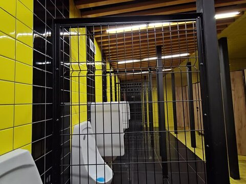 Row of urinals with a blue lid on the left urinal. The urinals are in a yellow room