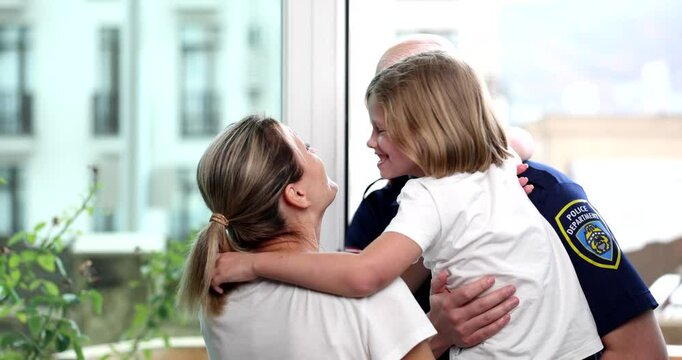Bald man in police uniform cheerfully enters apartment and hands daughter to worried mother. Moment of emotional family reunion after tough times