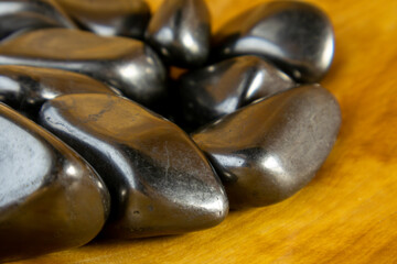 Pile of black rocks on a wooden surface. The rocks are all different sizes and shapes. Some are...