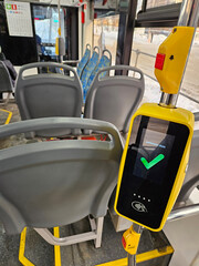 Yellow and black device with a green check mark on it. The device is on a bus. contactless payment...