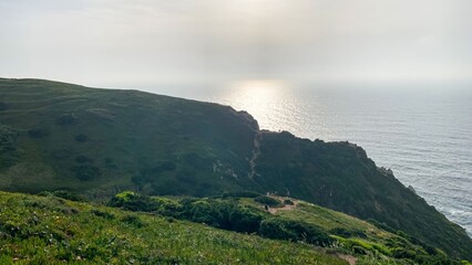 Sunlit mist kisses wild verdant cliffs, whispering secrets of Beltane's rebirth and the coastal All Souls' pilgrimage