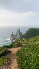 A solitary hiker, possibly Hispanic male, ventures along a lush cliffside path, evoking Dia de los Farolitos and Earth Day