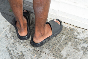 Lower body of an unidentified person standing on a paved street. Pedestrians.
