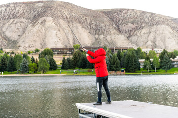 Nottingham lake park dock in Avon, Colorado cold morning with woman on fishing pier casting line at sunrise in small mountain village ski town city