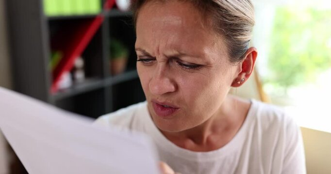 Woman strains to read document with brows furrowed and eyes squinting suggesting difficulty with poor vision. Struggle to decipher text on paper