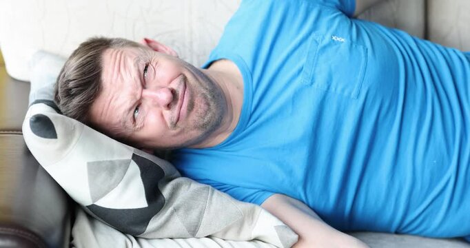 Exhausted man tries to rest on sofa after hard work day. Guy irritably covers head with huge pillow to block out loud sounds around distracting male
