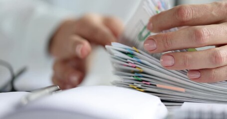 Female office worker browses through large documents stack secured with colorful paper clips. Person shows organized paperwork in office environment - Powered by Adobe