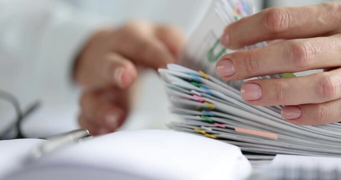 Female office worker browses through large documents stack secured with colorful paper clips. Person shows organized paperwork in office environment - Powered by Adobe