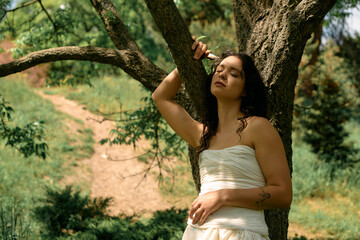 Curly-haired woman in a stylish white dress enjoys a peaceful summer day outdoors
