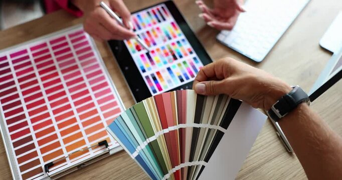 Designers discuss color palettes for project using digital tablet and color swatch. Professionals show collaborative process and color selection - Powered by Adobe