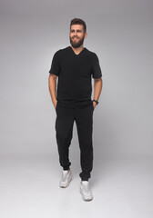young stylish bearded male nurse with long legs in black medical costume is standing in step with...