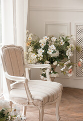 white armchair with spring flowers near the window in a classic interior near white wall background, free space