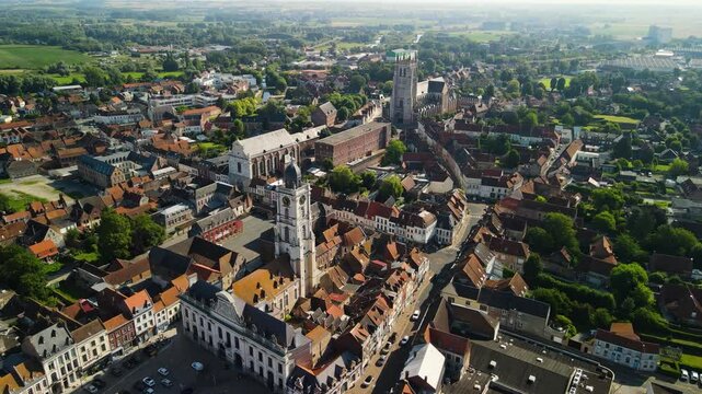 Aerial drone view of a historic northern French town with red-tiled rooftops, the UNESCO-listed bell tower, the baroque Jesuit chapel, and the gothic Saint-Pierre church. Shot in Aire-sur-la-Lys
