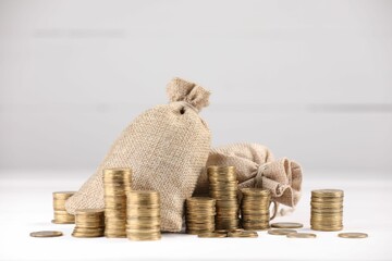 Bags and stacked coins on white table against light background