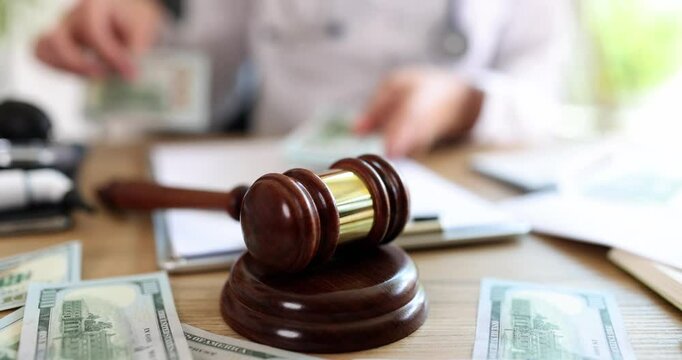 Female doctor counts bribe money near gavel and documents on desk. Representing corruption in healthcare office and medical malpractice lawsuits