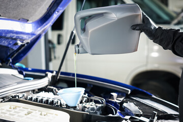 Worker pouring motor oil from canister into car engine, closeup