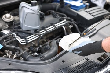 Worker checking motor oil level in car with dipstick, closeup