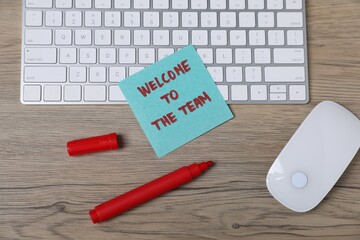 Sticky note with phrase Welcome To The Team, marker, computer keyboard and mouse on wooden table,...