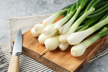 Fresh ripe green onions with cutting board and knife on grey textured table, closeup