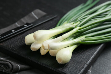 Fresh ripe green onions with cutting board and knife on black table, closeup