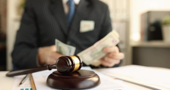 Lawyer counts dollar banknotes near judge gavel resting prominently on desk. Judicial system compromise and ethical challenges in legal profession