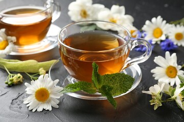 Aromatic herbal tea in glass cups, different flowers and mint on black table, closeup