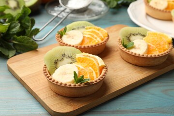 Tartlets with fruits and mint on light blue wooden table, closeup. Delicious dessert