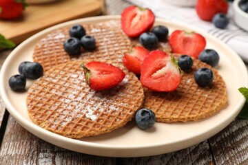 Tasty Dutch waffles (stroopwafels) and berries on wooden table, closeup