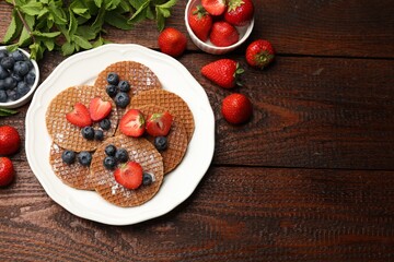 Tasty Dutch waffles (stroopwafels), mint and berries on wooden table, flat lay. Space for text
