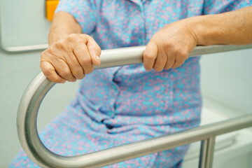 Asian elderly woman patient use toilet support rail in bathroom.