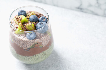 Delicious chocolate pudding with chia seeds, kiwi and blueberries in glass on light grey table,...