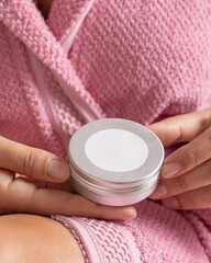 Woman in pink bathrobe holding body butter jar with a label in hands, Closeup, cosmetic mockup