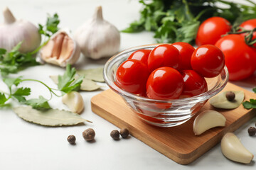 Tasty pickled tomatoes in glass bowl and spices on white table, closeup