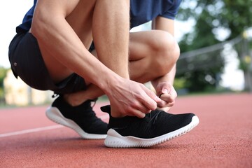 Man tying shoelace of black sneaker at stadium, closeup