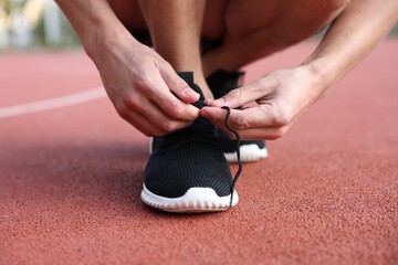 Man tying shoelace of black sneaker at stadium, closeup