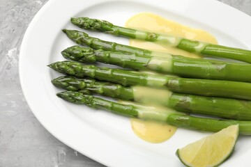 Tasty cooked asparagus served with sauce and lime on grey textured table, top view