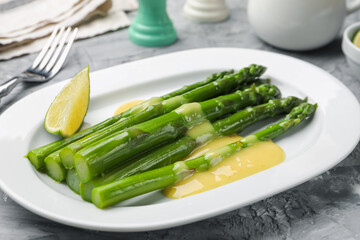 Tasty cooked asparagus served with sauce and lime on grey textured table, closeup