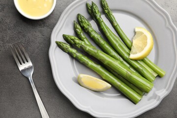 Tasty cooked asparagus served with lemon on grey table, flat lay