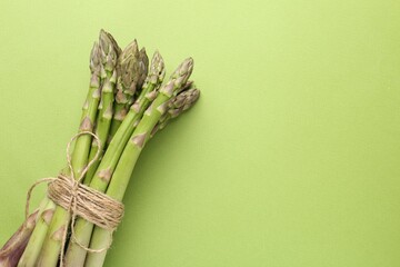 Tied raw asparagus on green background, top view. Space for text