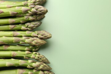 Fresh ripe raw asparagus on green background, closeup. Space for text