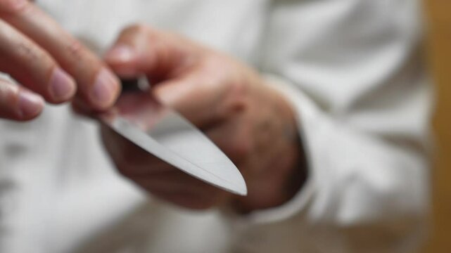 A man touches a sharp blade on a knife before cutting something.
A close-up of a sharp knife in the hand of a master.
A chef with a sharp knife in the kitchen