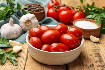 Tasty pickled tomatoes in bowl and ingredients on wooden table, closeup