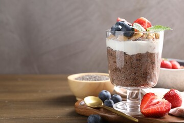 Delicious chocolate pudding with chia seeds, nuts and berries in glass on wooden table, closeup....