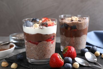 Delicious chocolate puddings with chia seeds, nuts and berries in glasses on grey table, closeup