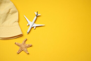 Airplane model, hat and starfish on yellow background, flat lay. Space for text