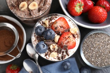 Delicious chocolate puddings with chia seeds, nuts and berries in glasses on grey table, flat lay